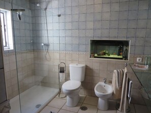 Une salle de bain avec une douche à parois de verre, des toilettes, un bidet et un petit aquarium fixé au mur.