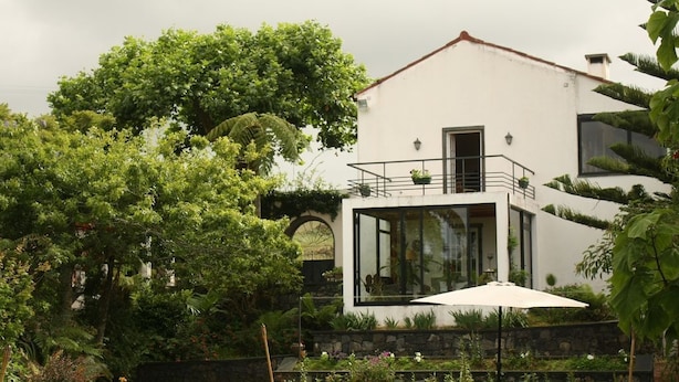 Une maison moderne dotée d’une véranda en verre, d’une pelouse et d’un fauteuil de jardin.