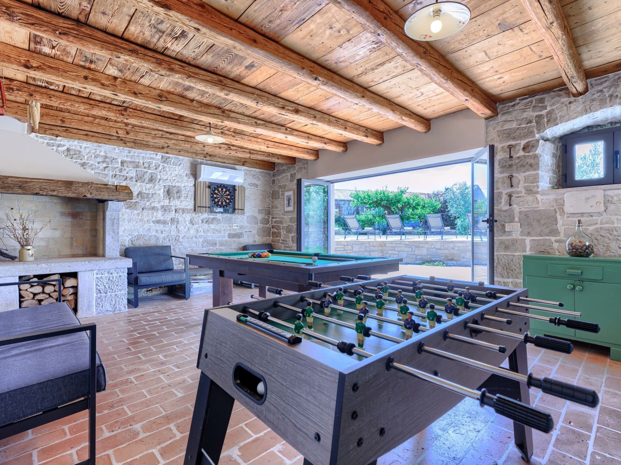 Un espace de loisirs intérieur accueillant, doté d’un baby-foot, d’une table de billard et d’un jeu de fléchettes, avec des murs en pierre et des poutres en bois.
