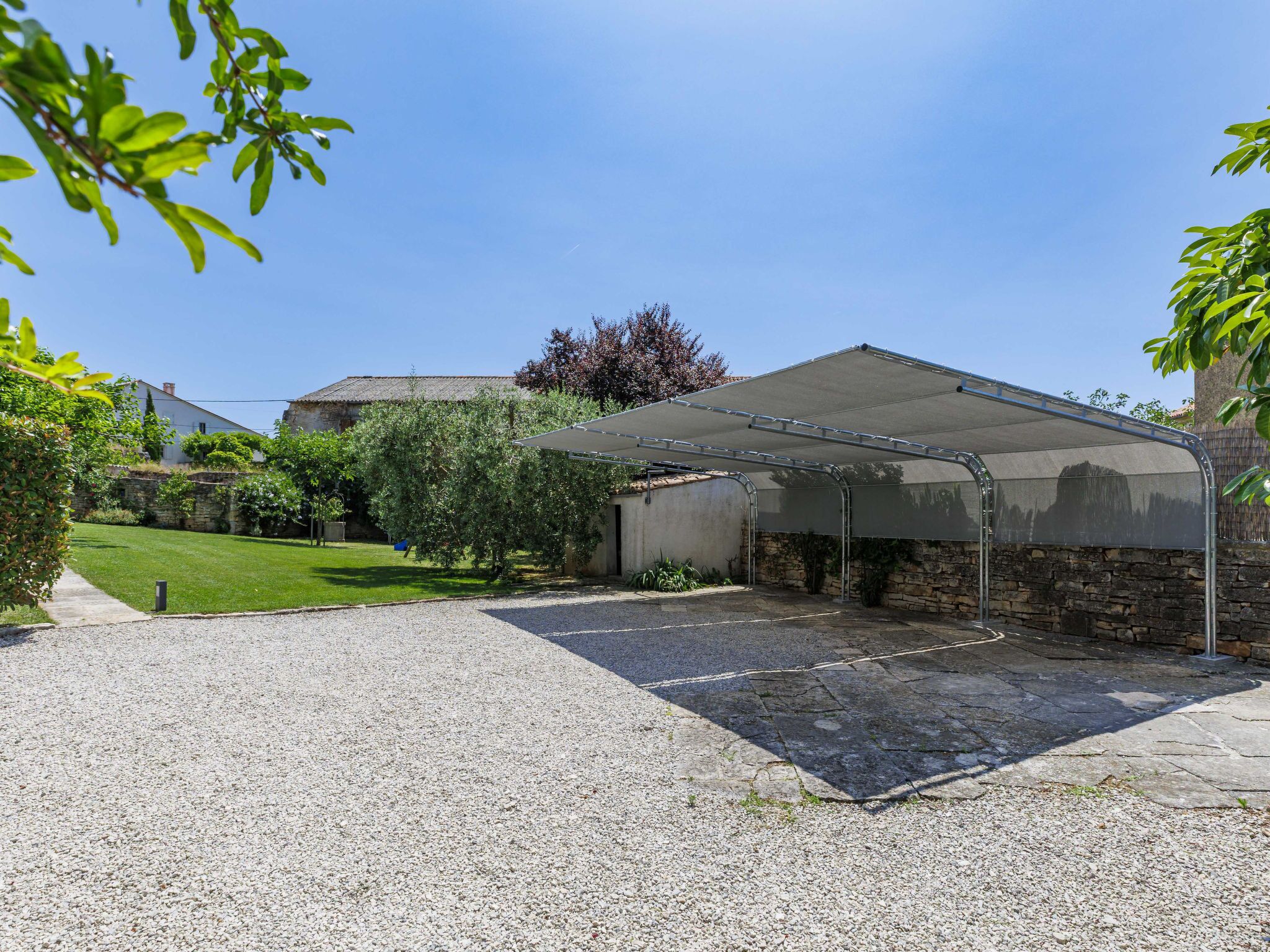 A covered outdoor area with a gravel driveway leading to a stone building.