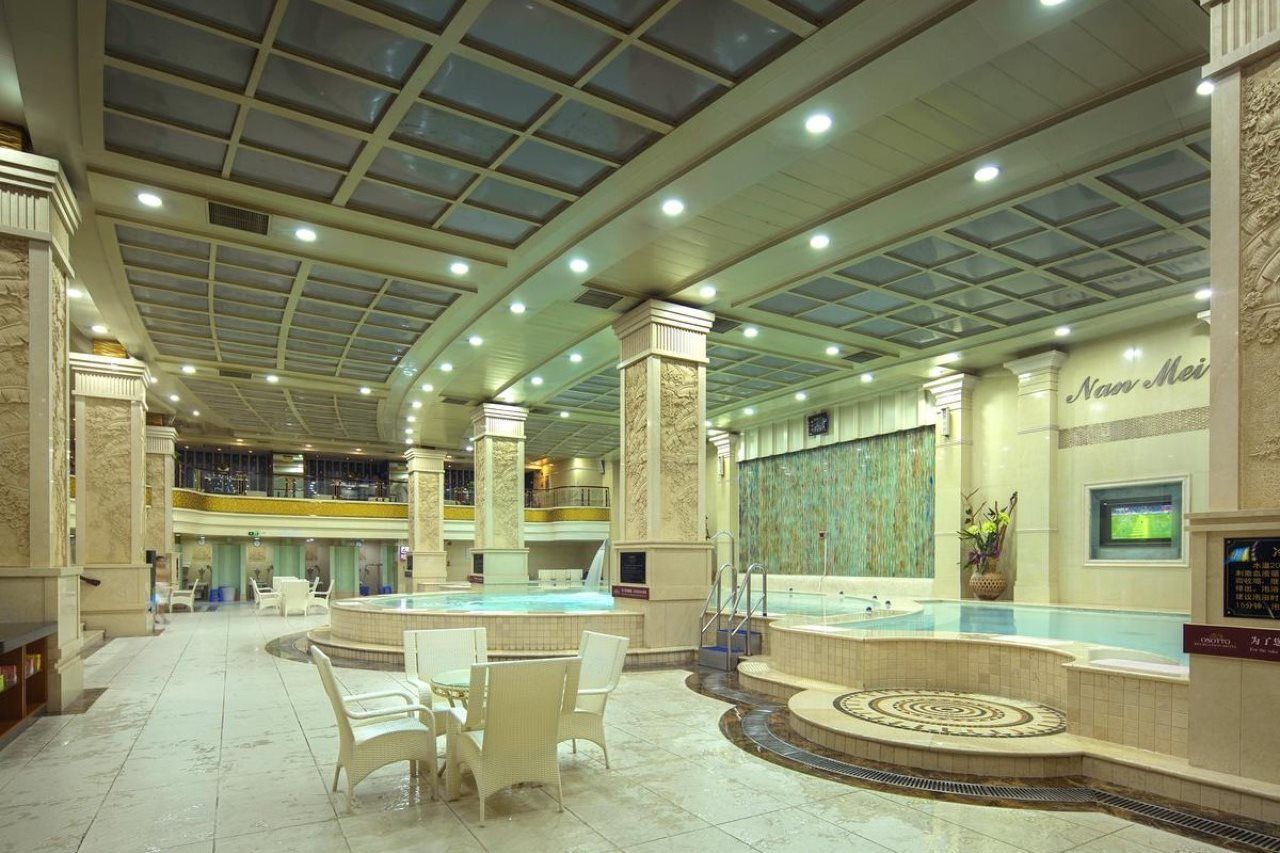 Amplia zona de piscina interior con varios niveles, áreas de descanso y una gran pared con pantalla.