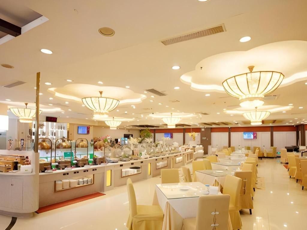 Espaço de refeições de hotel com várias mesas, cadeiras, balcão de buffet e luminárias de teto modernas.