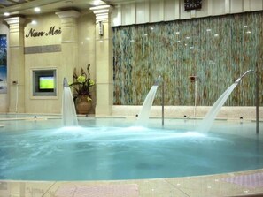 Un hall d’hôtel avec une piscine dotée de trois jets d’eau, un comptoir de réception et un mur décoratif.
