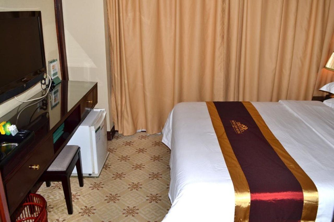 A hotel room with a bed, a desk with a television, and a small refrigerator.