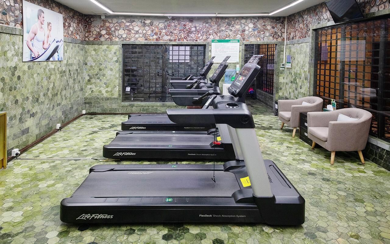 Un gimnasio con cintas de correr, sillas de ejercicio y un piso estampado.