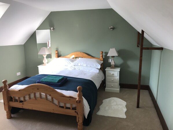 A bedroom with a wooden bed, white bedding, a nightstand with a lamp, and a white furry rug. - Torran Cottage - The Highland Cottage with a Piano (Stoer)