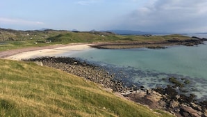 Eine Küstenlandschaft mit Sandstrand, felsigem Ufer und grasbewachsenen Hügeln.