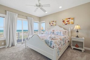 A bedroom with a bed, a ceiling fan, a nightstand, a lamp, and a view of the ocean.
