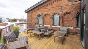 En træterrasse med udendørs møbler, murstensvægge og store vinduer.