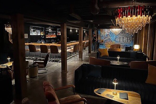 A dimly lit lounge area with leather sofas, wooden tables, and a bar in the background.