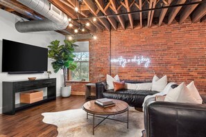 A modern living room with a brick wall, a black leather sofa, a round coffee table, and a large potted plant.