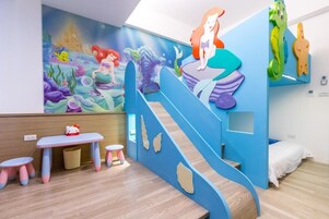 Un espace de jeux pour enfants avec une fresque murale, un toboggan et une petite table sur laquelle est posé un jouet Hello Kitty.