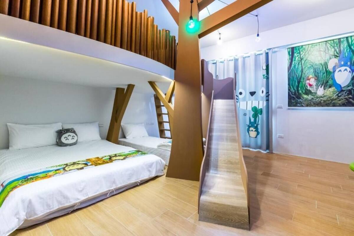A bedroom with a bunk bed, a ladder, a bed with a colorful blanket, and a wall with a forest-themed painting.