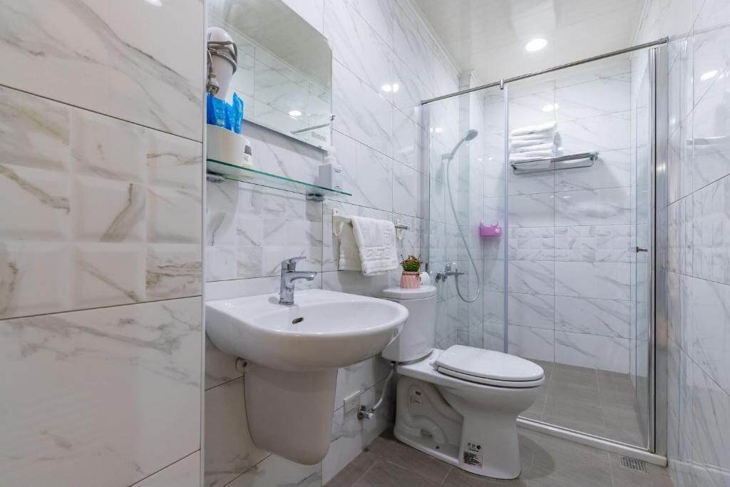 Un baño moderno con cabina de ducha de vidrio, lavamanos pedestal y retrete.
