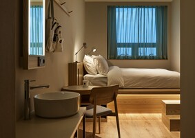 Un dormitorio moderno con cama, mesita de noche, lámpara y vistas al exterior a través de una ventana.
