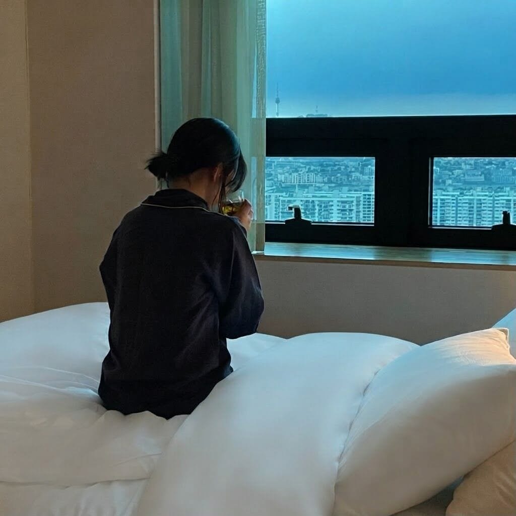 A person sitting on a bed with a window view of a cityscape.