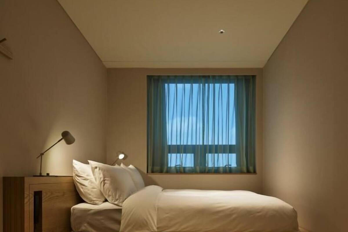 A modern bedroom with a loft bed, wooden flooring, a desk, and a window with curtains.