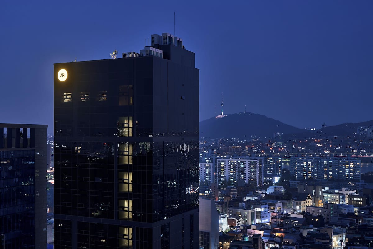 A high-rise building with illuminated windows, a prominent 'AR' sign, and a cityscape with distant mountains in the background.