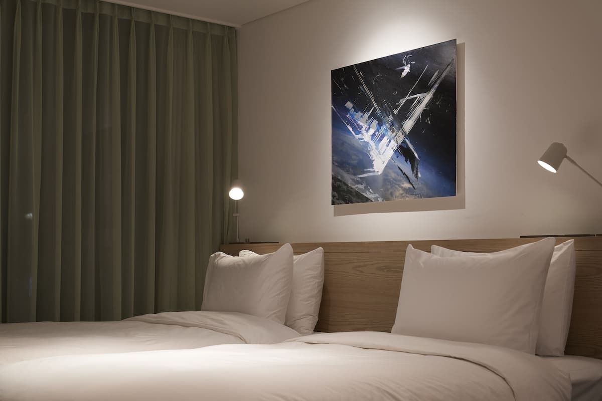 A hotel room with a large bed, a wooden headboard, a painting of a bridge, and a lamp.