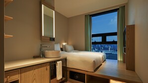 A modern hotel room with a large bed, a vanity with a mirror, a sink, and a view of the cityscape through a large window. - Anteroom Seoul (Seoul)
