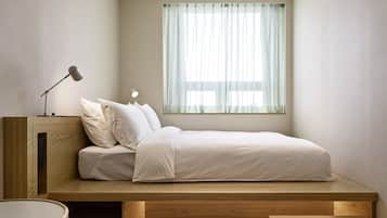 A compact bedroom with a built-in bed, a bedside table, a lamp, and a window with sheer curtains.