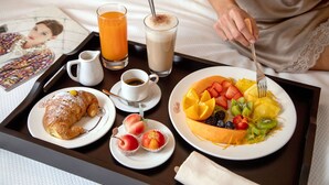 Bandeja de desayuno con croissant, jugo, café y una fuente de fruta.