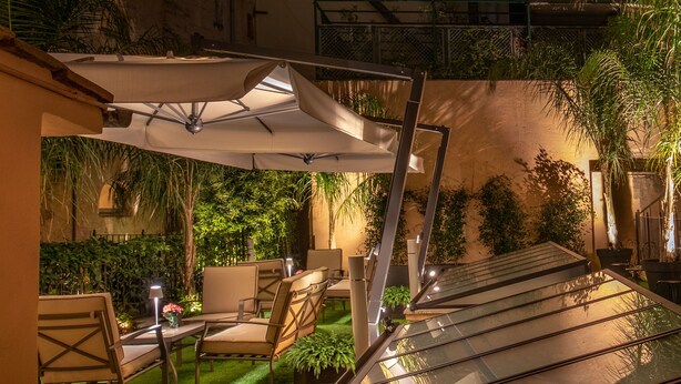 Un patio al aire libre con mesa de vidrio, sillas y una sombrilla blanca.