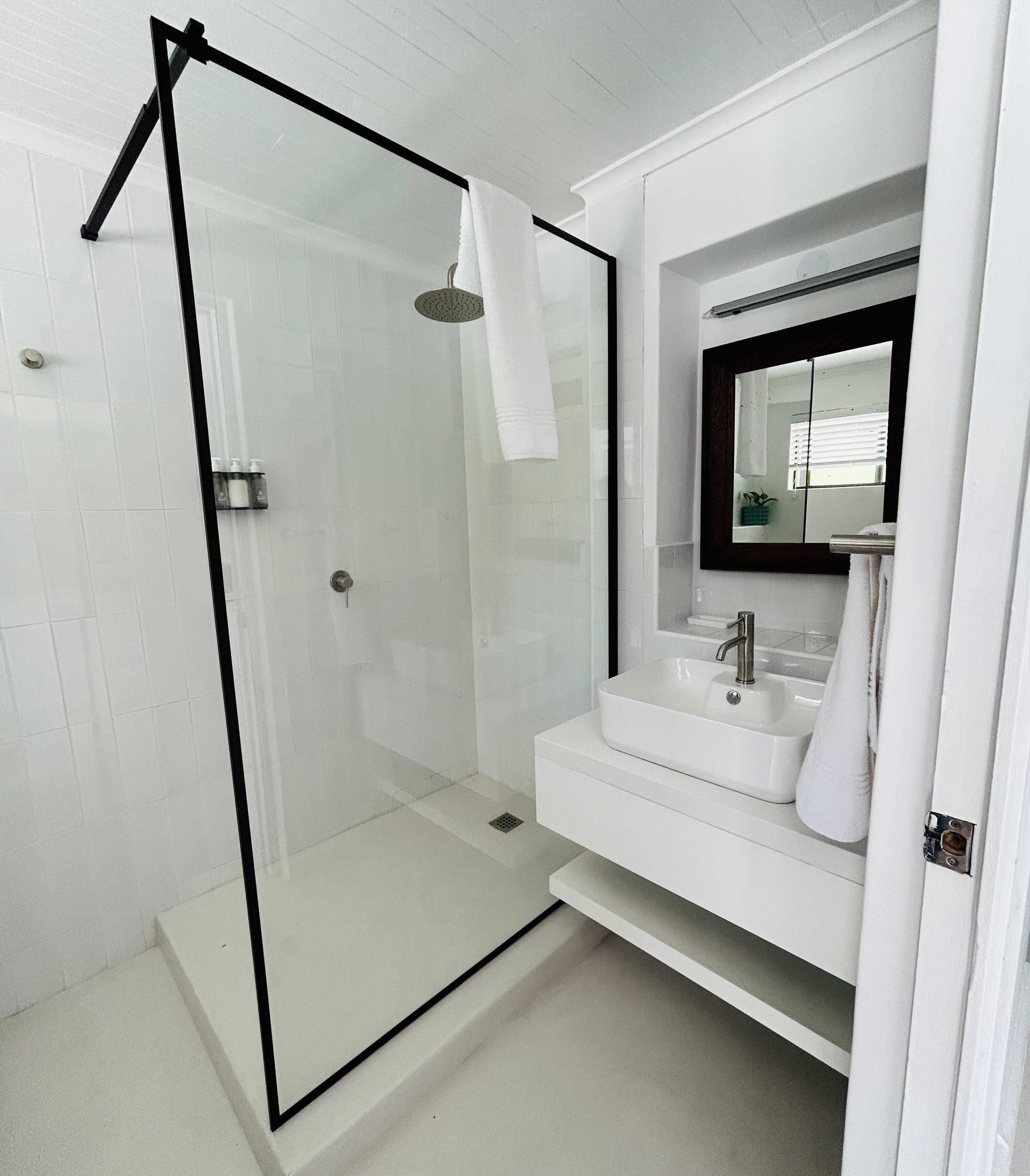 Une salle de bain moderne avec une douche à l’italienne en verre, un lavabo blanc et un grand miroir.