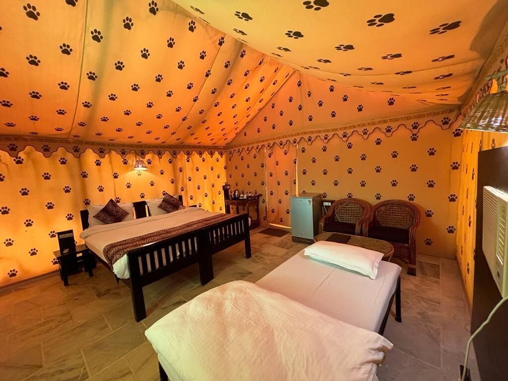 Une chambre avec deux lits, une petite table, une chaise, un téléviseur et un mur orné d’un motif représentant des empreintes de pattes.