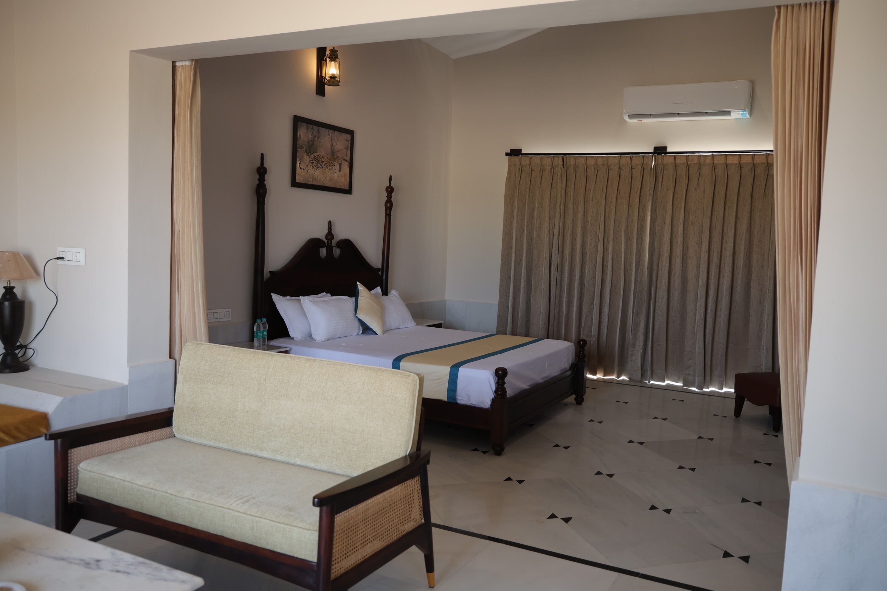 A hotel room with two beds, a sofa, a lamp, and an air conditioning unit.