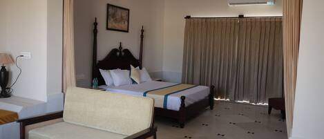 A hotel room with two beds, a sofa, a lamp, and an air conditioning unit.