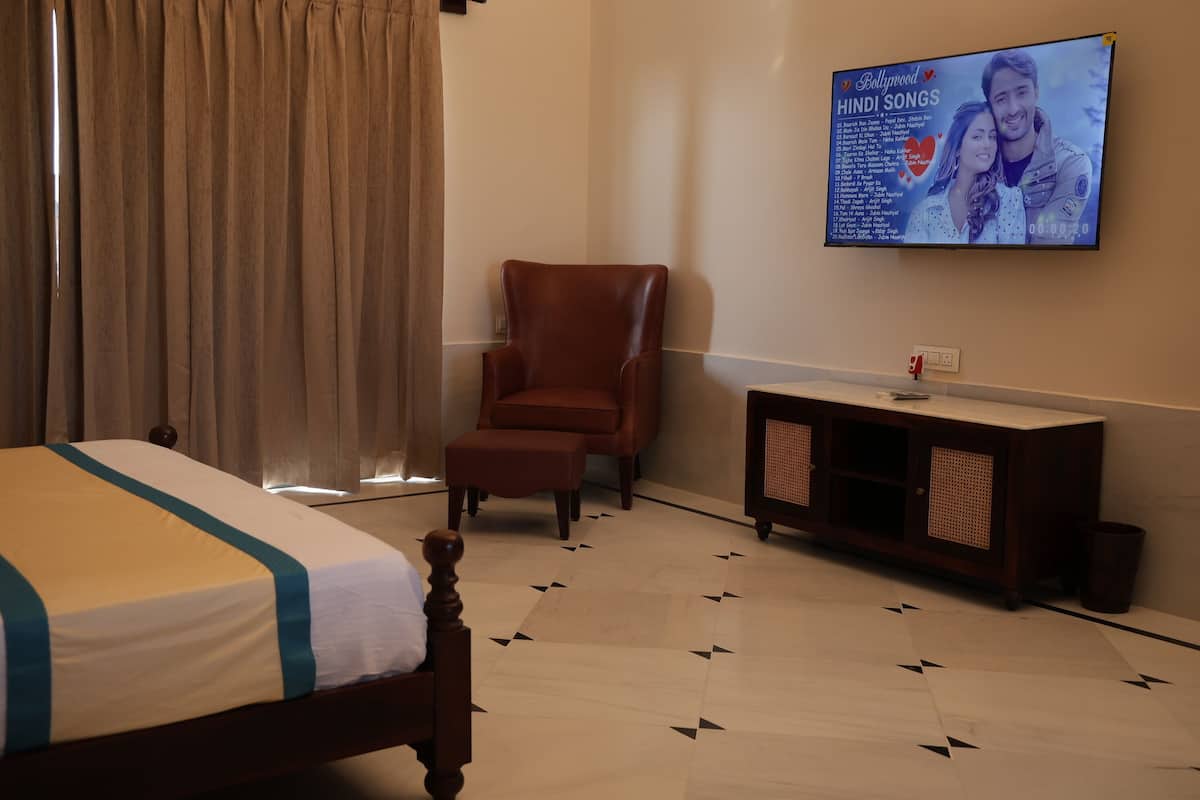 Una habitació d'hotel amb un llit, un sofà d'armariadura de pell marró, una televisió que mostra cançons hindi de Bollywood i un petit armari.