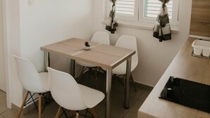 Una habitación pequeña y limpia con una mesa de comedor, sillas blancas, un ventanal con cortinas a rayas y una planta pequeña sobre la mesa.