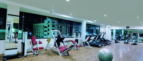 Un gimnasio con máquinas de cardio, equipo de entrenamiento de fuerza y una pelota de ejercicio grande.
