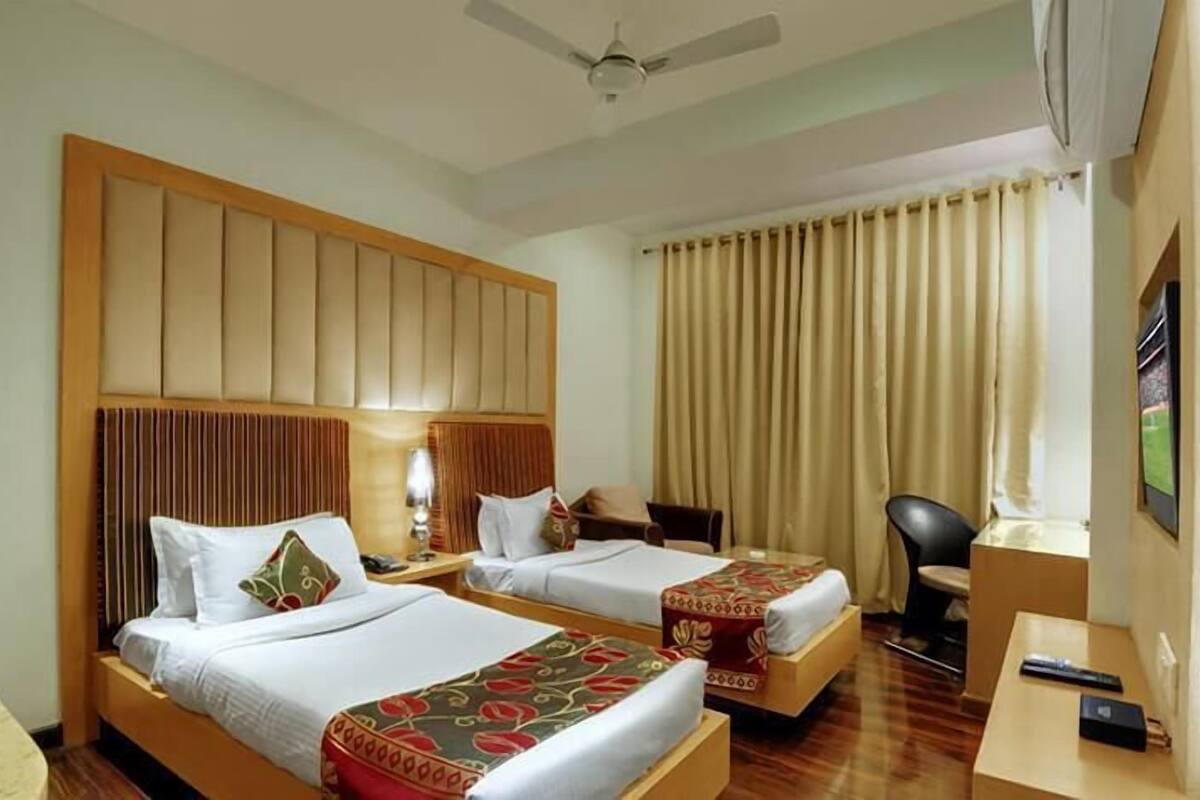 Une chambre d’hôtel avec deux lits, un bureau, une chaise, un ventilateur de plafond et une fenêtre avec des rideaux.