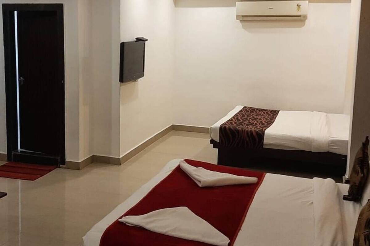Une chambre d’hôtel avec un canapé, un lit recouvert d’une couverture rouge, une petite table et un téléviseur.