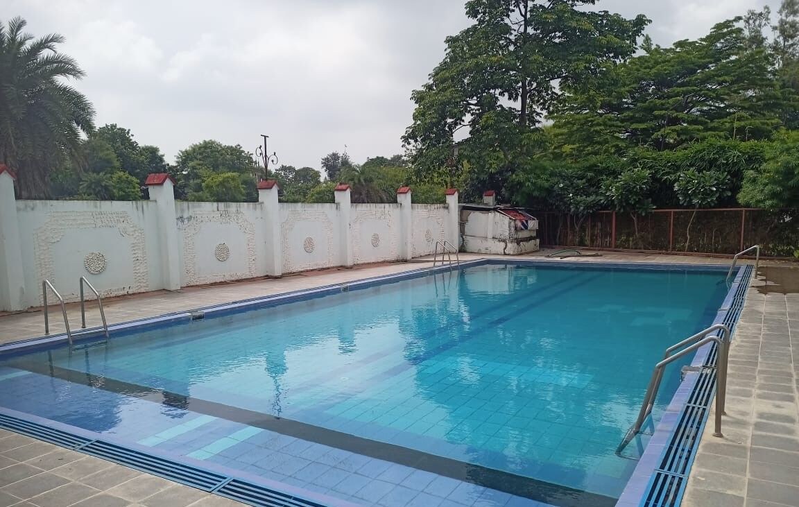 A rectangular swimming pool with clear blue water, surrounded by a white wall with decorative patterns and a metal ladder.