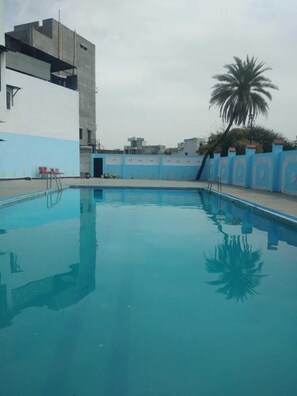 Una piscina con bordo piastrellato di blu, una palma e un edificio con facciata blu e bianca.