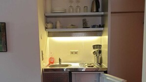 A compact kitchen with a built-in refrigerator, a sink, and shelves above for storage.