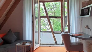 A room with a sloped ceiling, a desk with a chair, a sofa, and a small table.
