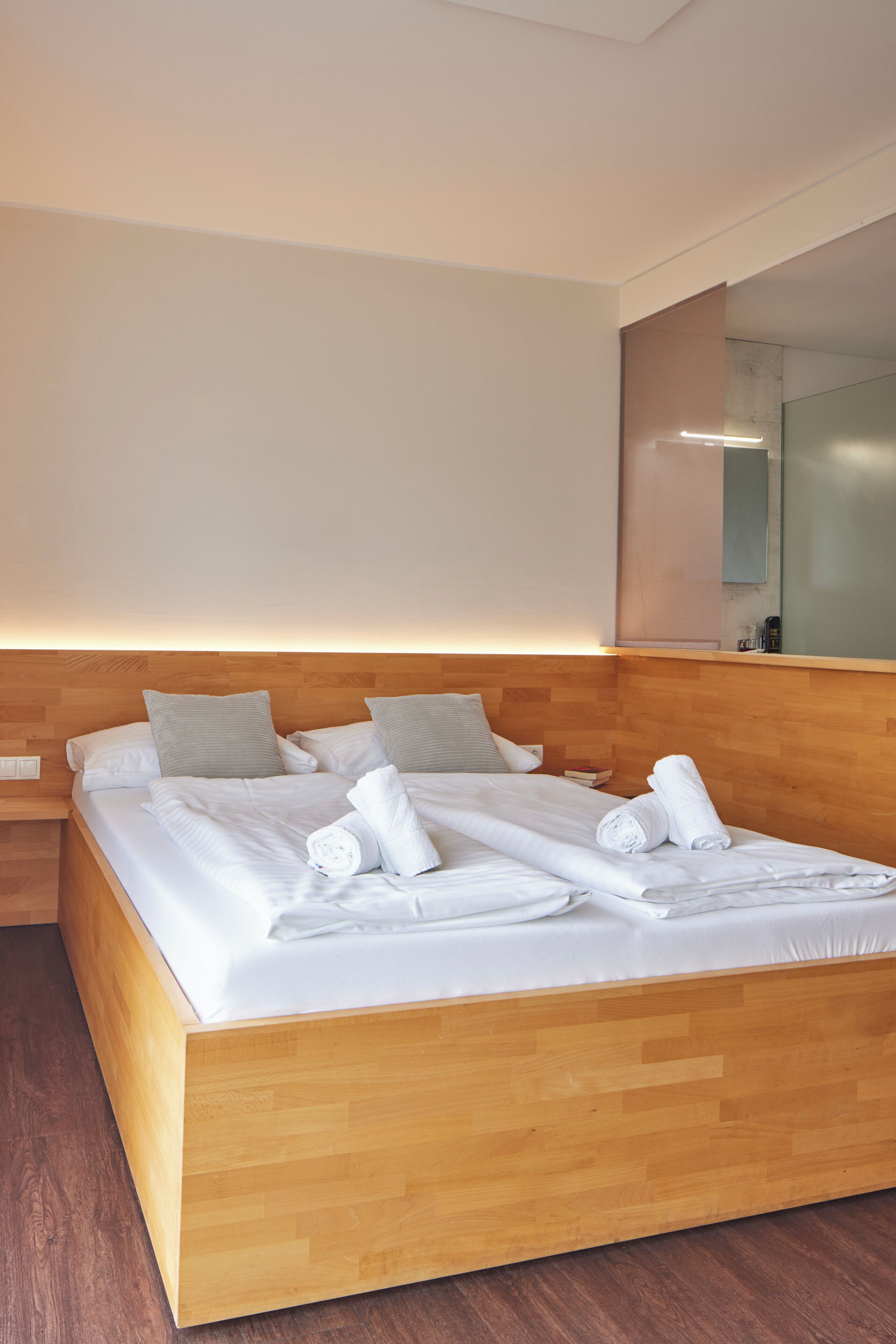 Una cama doble bien hecha con almohadas, un cabecero de madera y una mesita de noche con una lámpara.