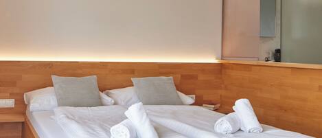 Una cama doble bien hecha con almohadas, un cabecero de madera y una mesita de noche con una lámpara.