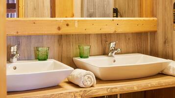 A bathroom with two white sinks, green glass cups, a towel, and a wooden wall.