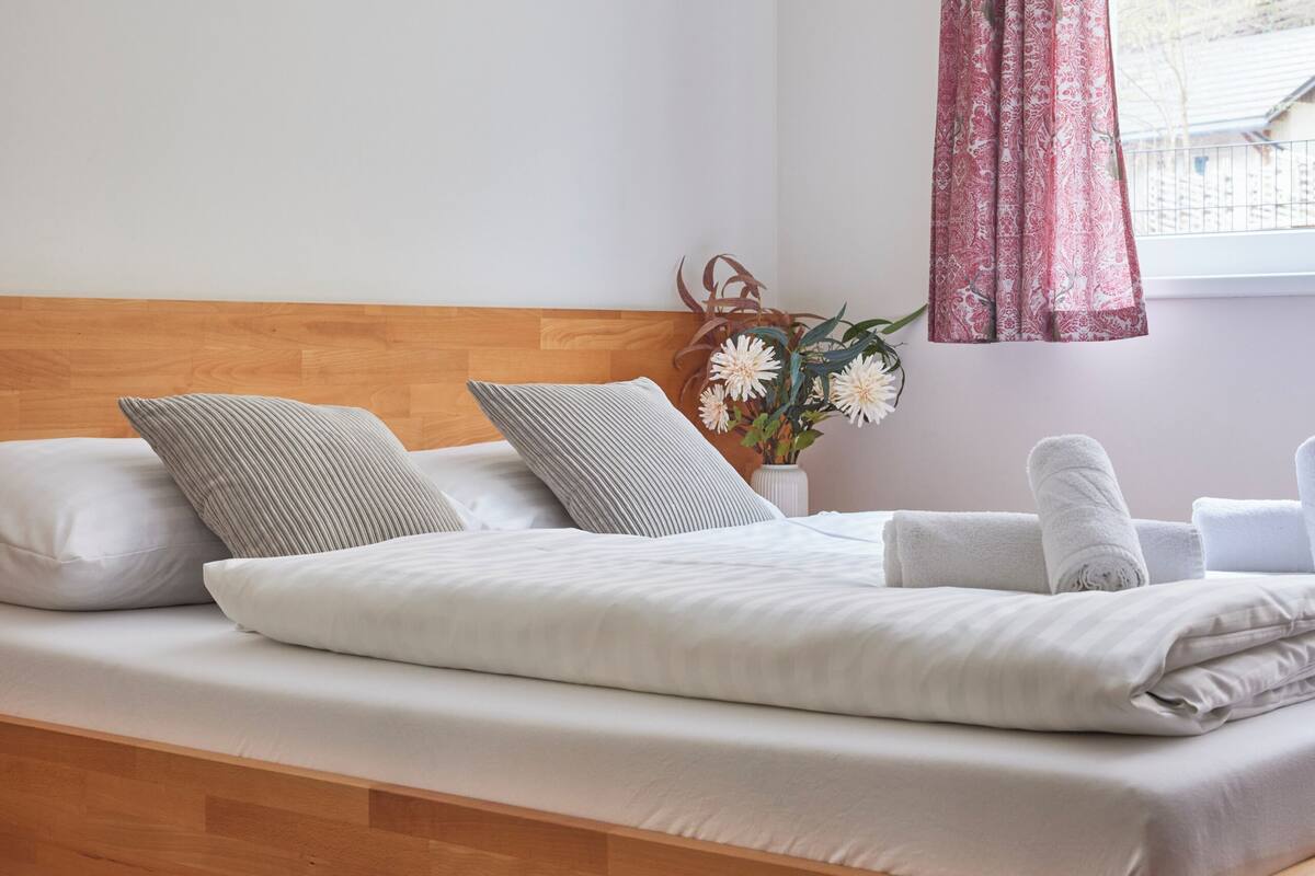 Un lit avec une tête de lit en bois, une literie blanche et un vase rempli de fleurs.