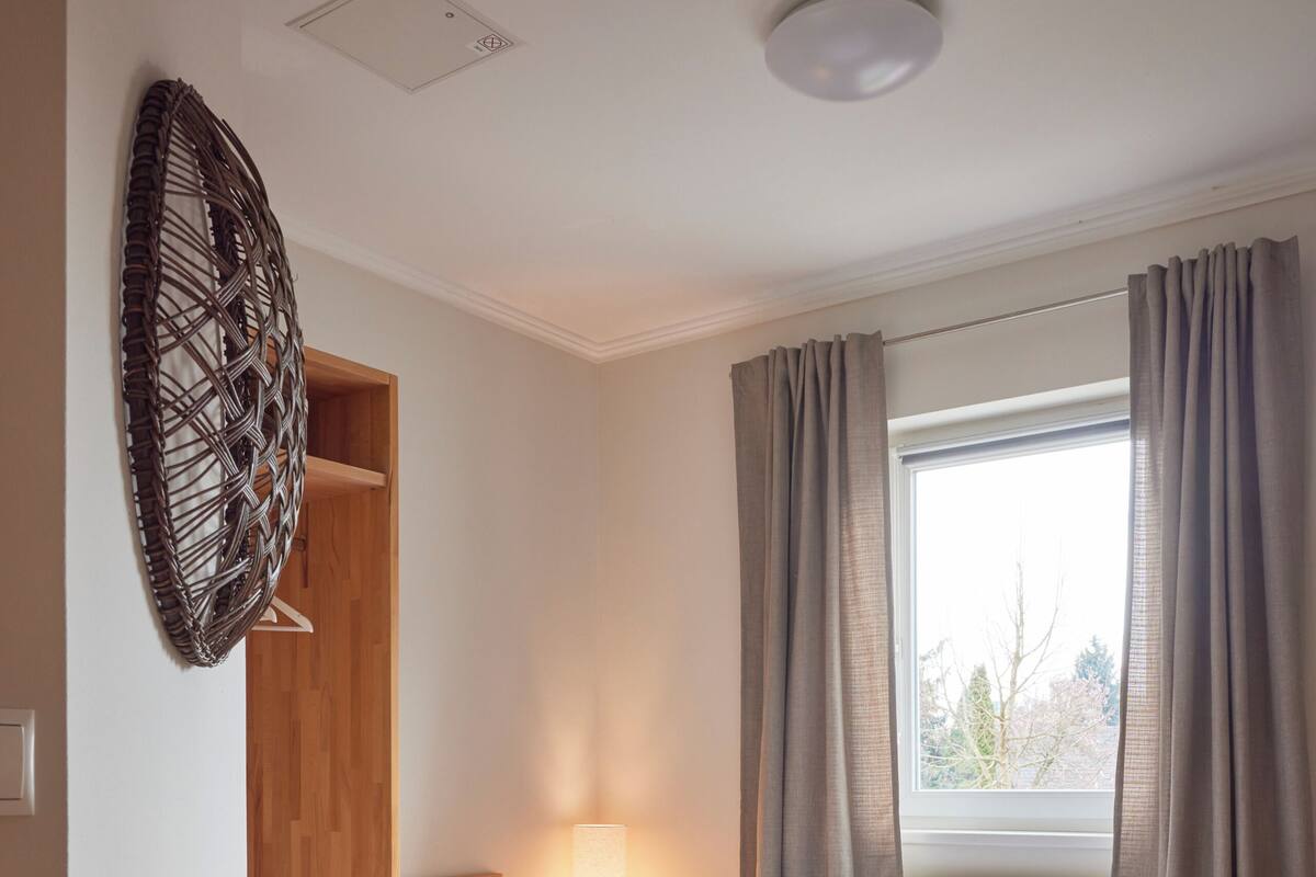 Une chambre à coucher avec un lit en bois, une table de chevet, une armoire, une fenêtre avec des rideaux et un radiateur.