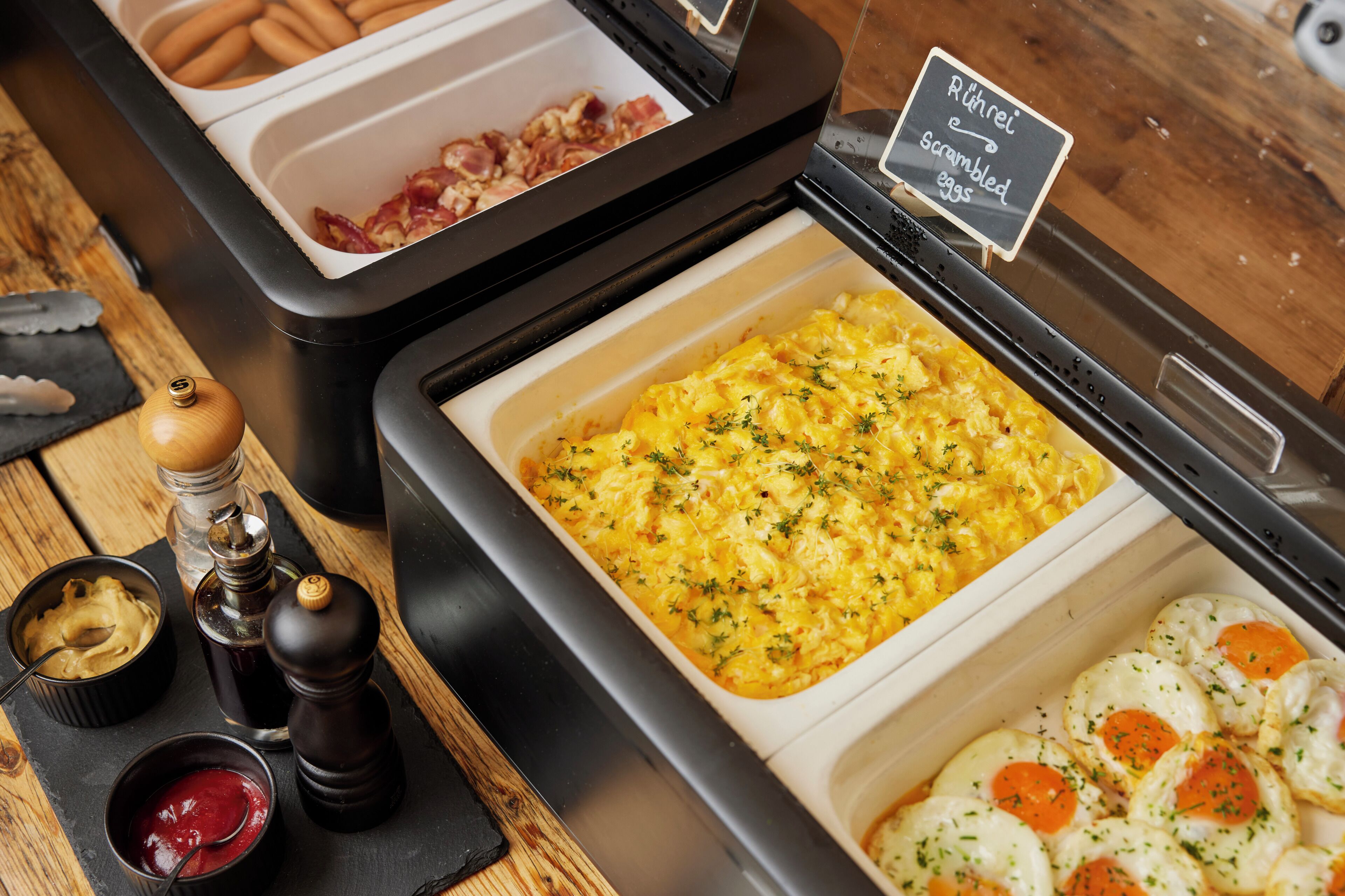 Ein Buffet mit Rührei, Speck und einem Schild, das Rührei anzeigt.