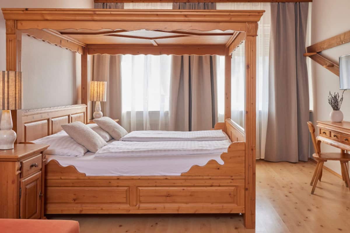 Un lit à baldaquin en bois, une table de chevet en bois avec une lampe, un bureau en bois avec un miroir et une chaise.