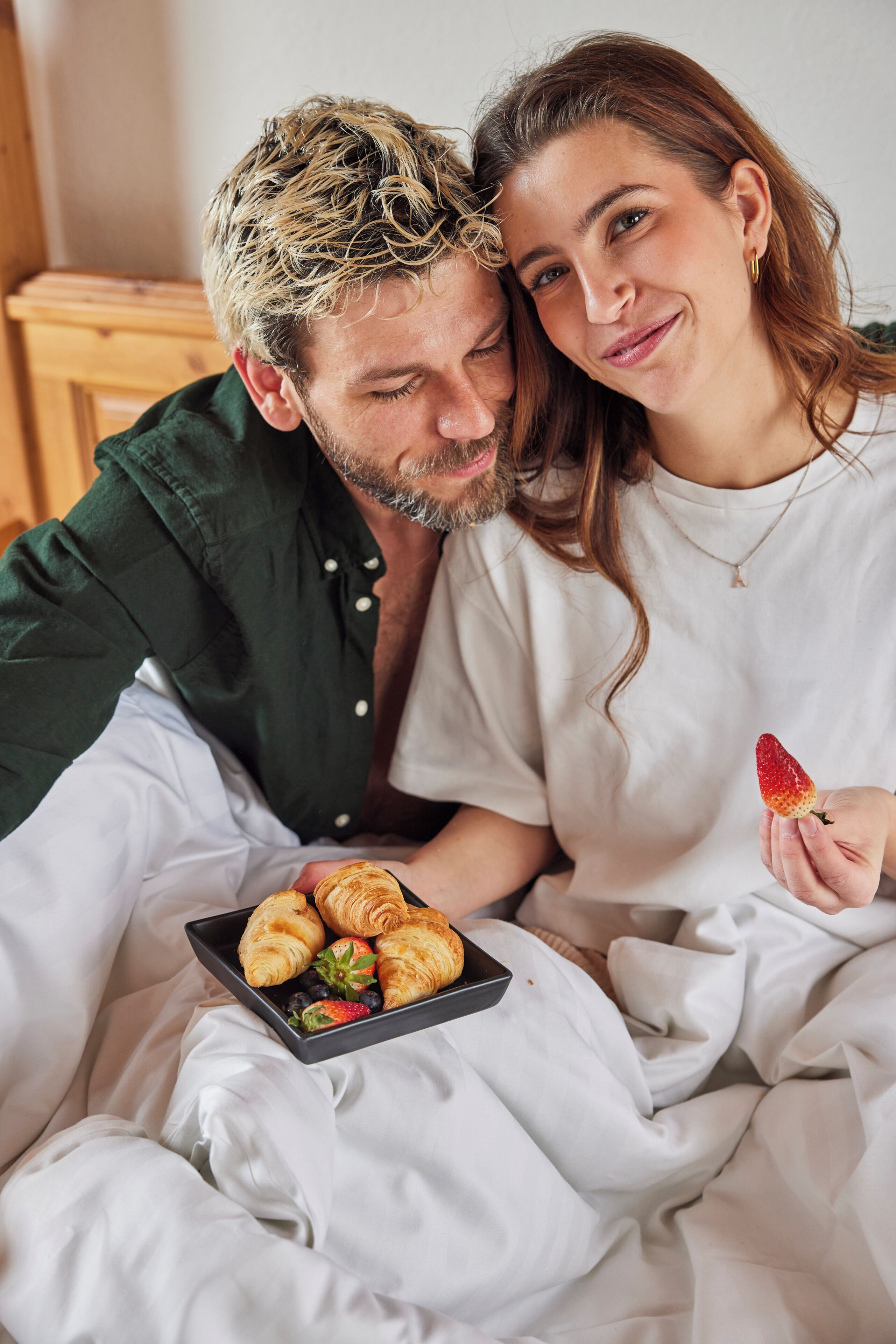 A couple in bed with a tray of croissants and strawberries.