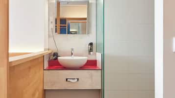 A modern bathroom with a white sink, a mirror, and a glass shower enclosure.