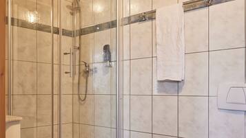 Un baño con ducha de mampara de vidrio, inodoro y cubo de basura.